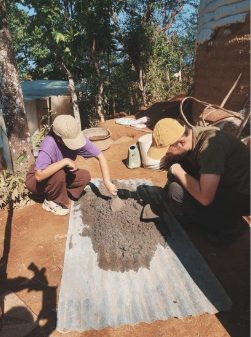 Two participants preparing an earth mix on a metal sheet outdoors in Nepal