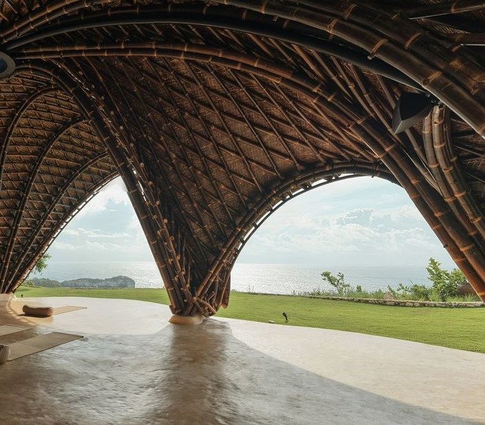 A polished earthen floor under a woven bamboo dome, opening onto a green landscape
