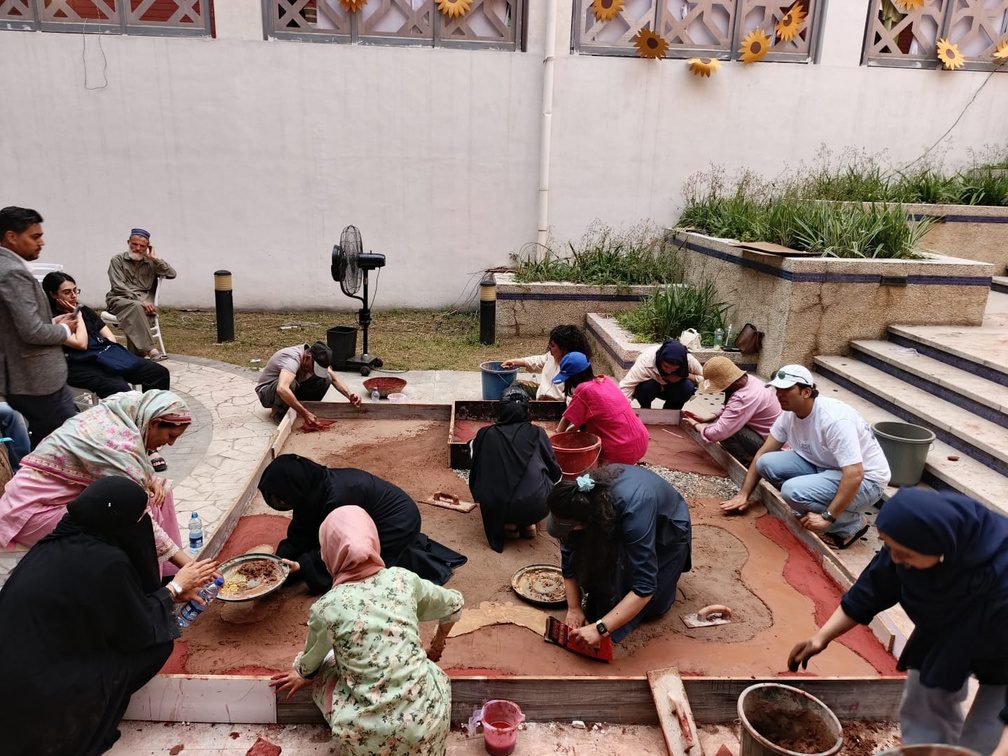 Participants laying an earthen floor together in a courtyard